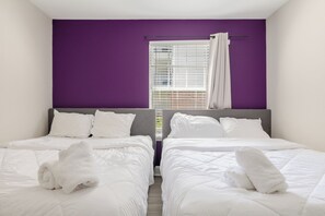 Une chambre double avec deux lits, du linge de lit blanc et un mur d’accent de couleur violette.