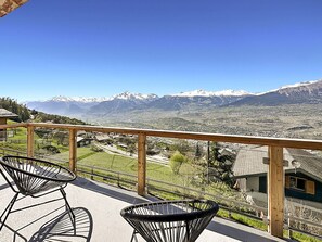 A balcony with two wicker chairs, a wooden railing, and a view of a mountain range with snow-capped peaks. - Chalet Commaraf! - Swiss Alp 4 Vallées by Interhome (Savièse)
