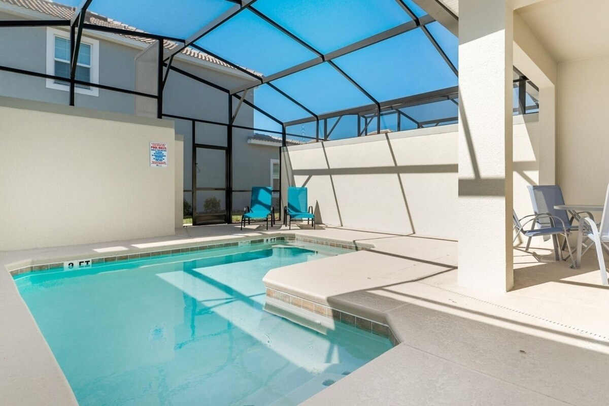 A swimming pool with a glass ceiling, blue chairs, and a pool table.