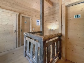 Ein holzgetäfelter Innenbereich mit einer rustikalen Holzgeländer, nummerierten Türen und einer Wandleuchte.