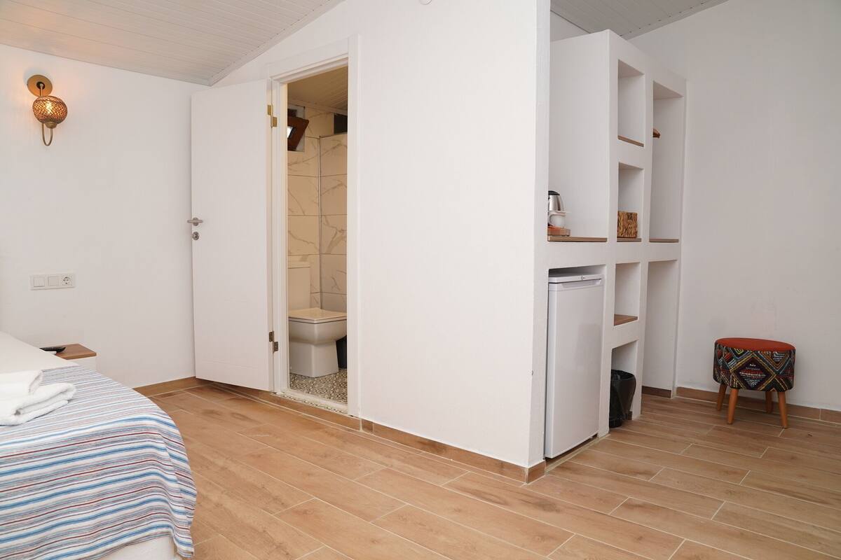Ein Schlafzimmer mit Bett, Schrank, einem kleinen Hocker und einem Badezimmer mit Dusche und Toilette.