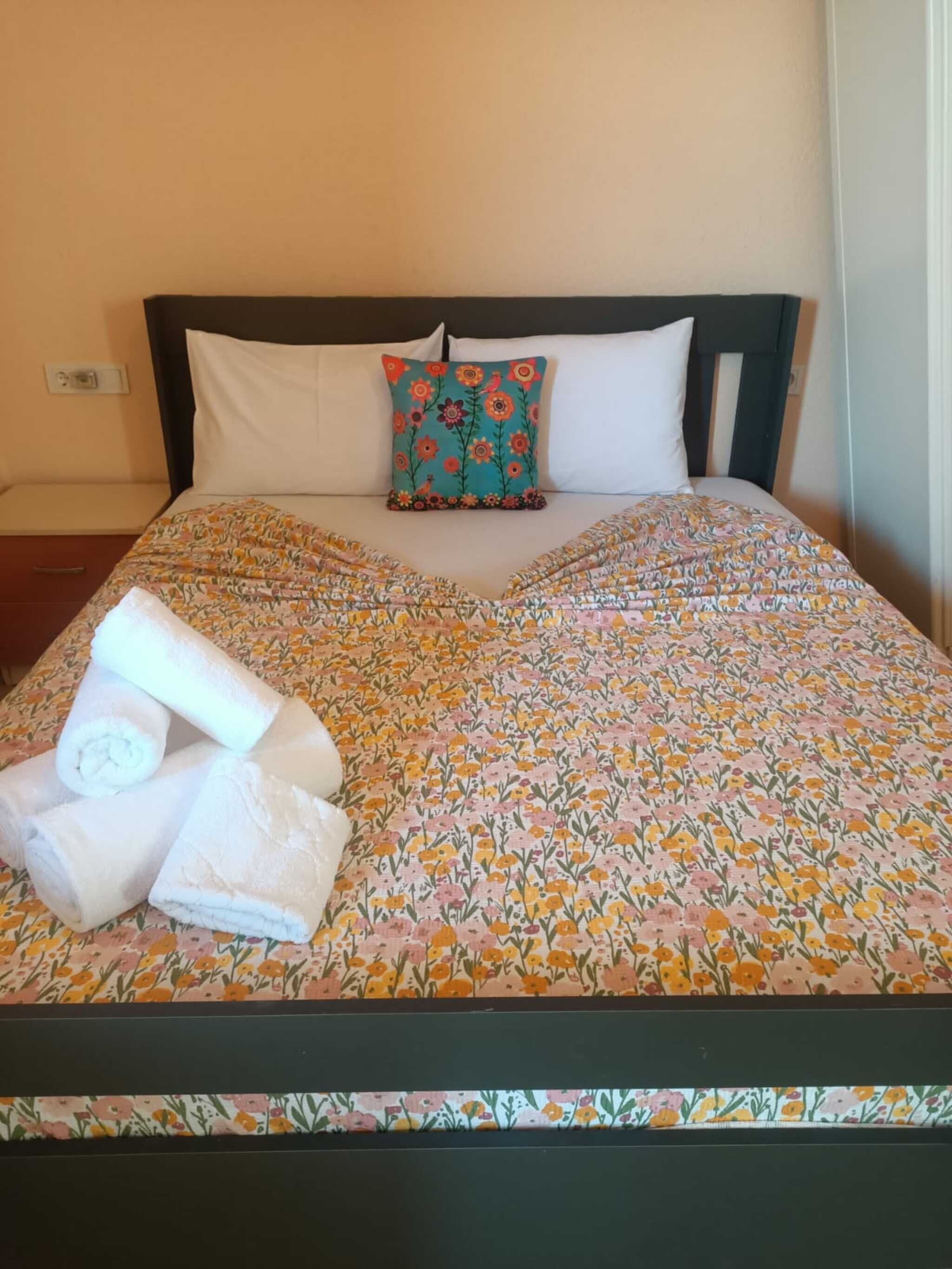 A bed with a floral bedspread, two pillows, and rolled towels.