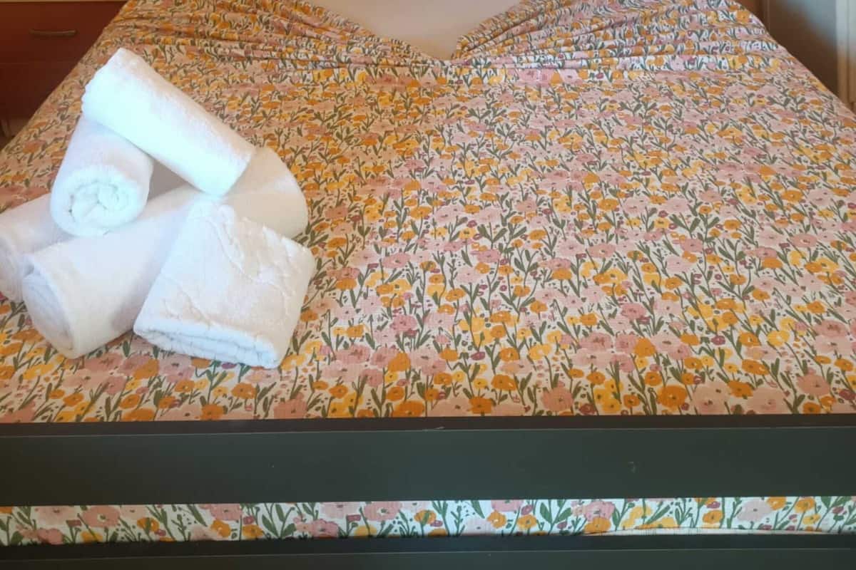 A bed with a floral bedspread, two pillows, and rolled towels.