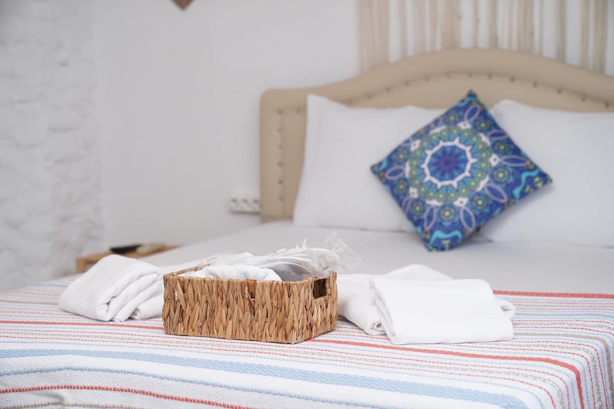 A neatly made bed with a striped bedspread, a woven basket with towels, and a decorative pillow.