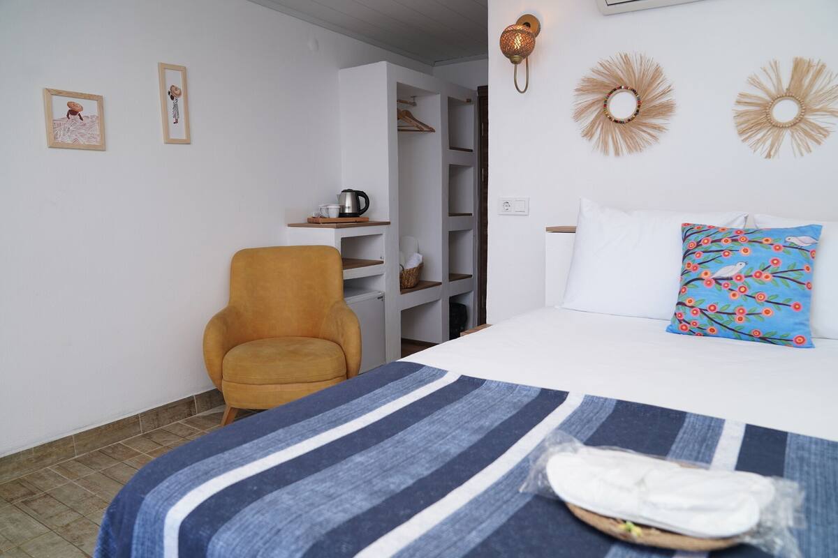 Ein Schlafzimmer mit einem Bett, einem Sessel, einem Regal mit Gegenständen und einem Kleiderschrank.