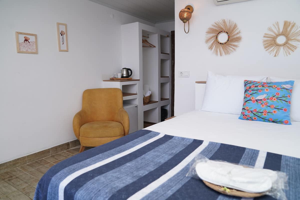 A bedroom with a bed, a chair, a shelf with items, and a wardrobe.
