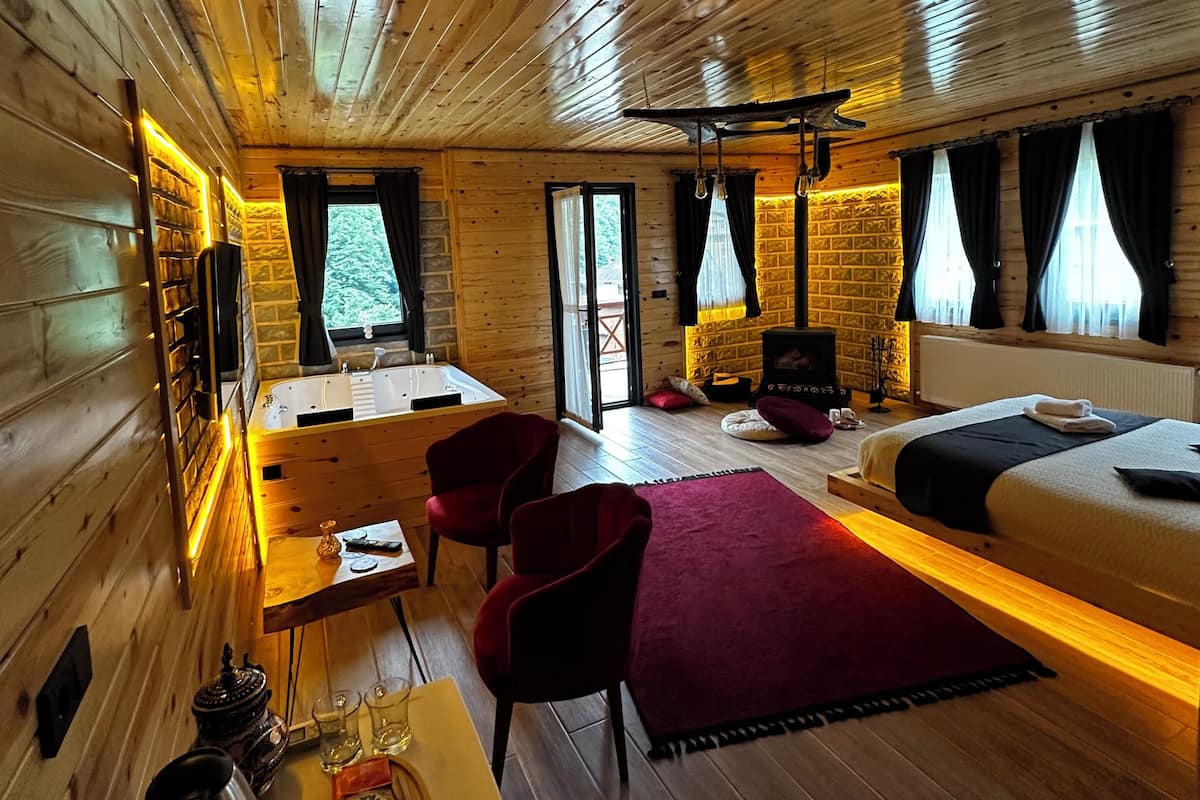A wooden cabin interior with a bed, seating area, and a fireplace.