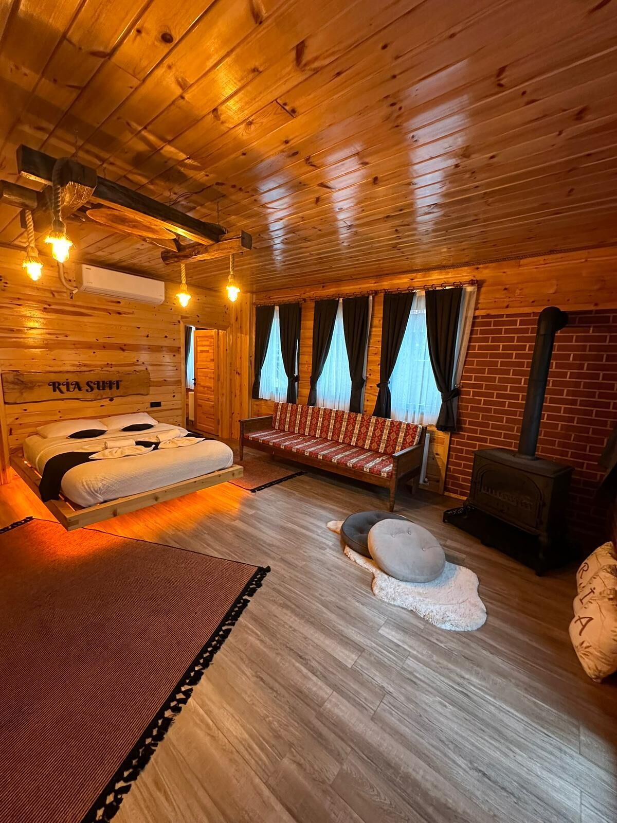 A wooden cabin interior with a bed, sofa, and a fireplace.