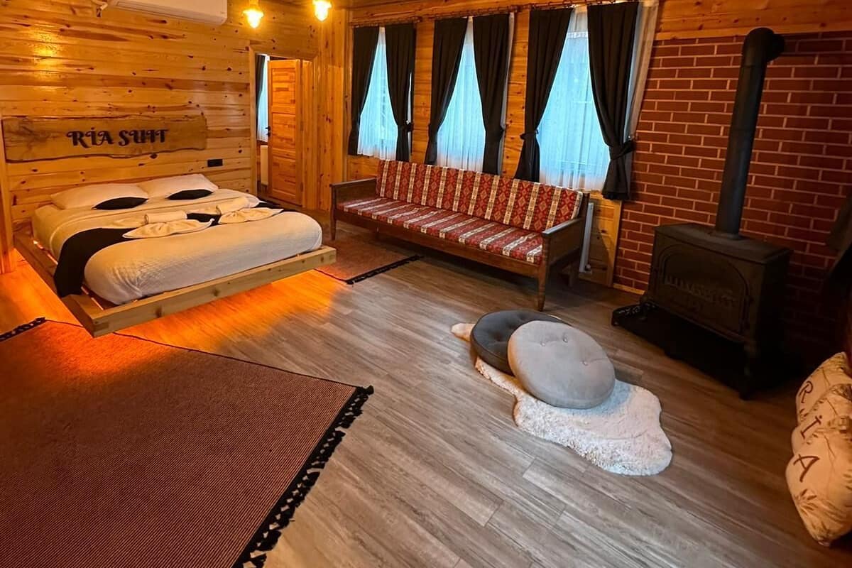A wooden cabin interior with a bed, sofa, and a fireplace.