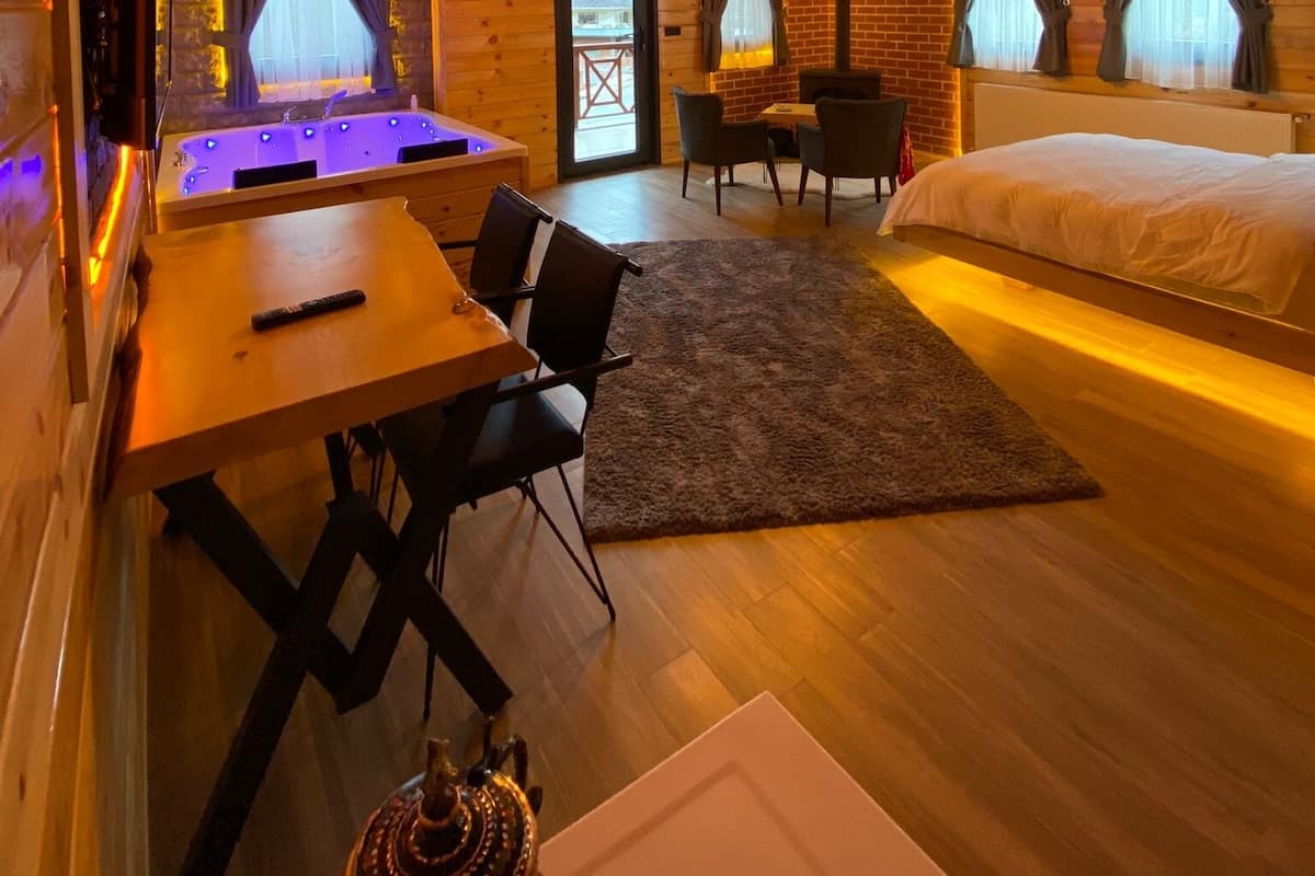 A wooden cabin interior with a bed, a dining area, a small kitchen, and a hot tub.