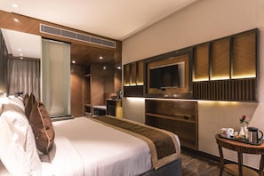 Een hotelkamer met een groot bed, een aan de muur bevestigde televisie, een bureau met stoel, en een klein tafeltje met een koffiezetapparaat en een bloem.