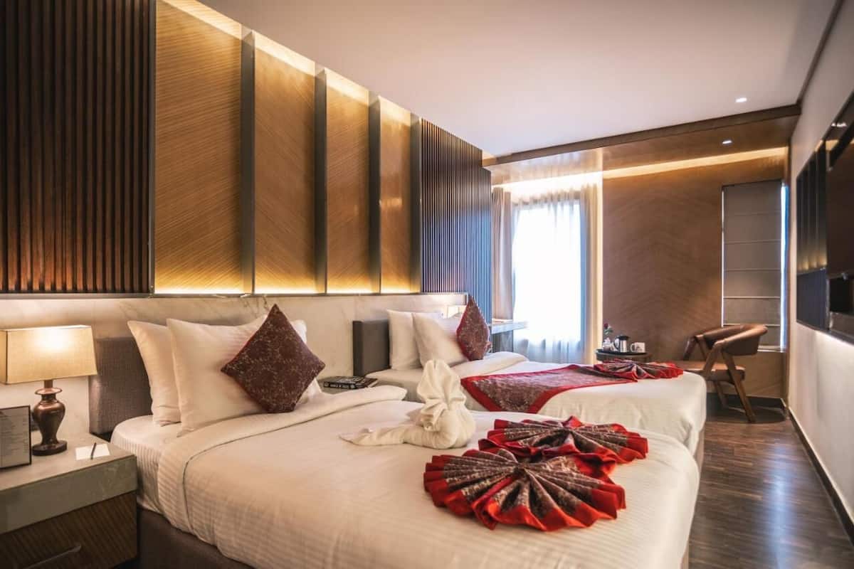 A hotel room with a large bed, a bedside table with a lamp, a flat-screen TV, and a seating area with a chair.