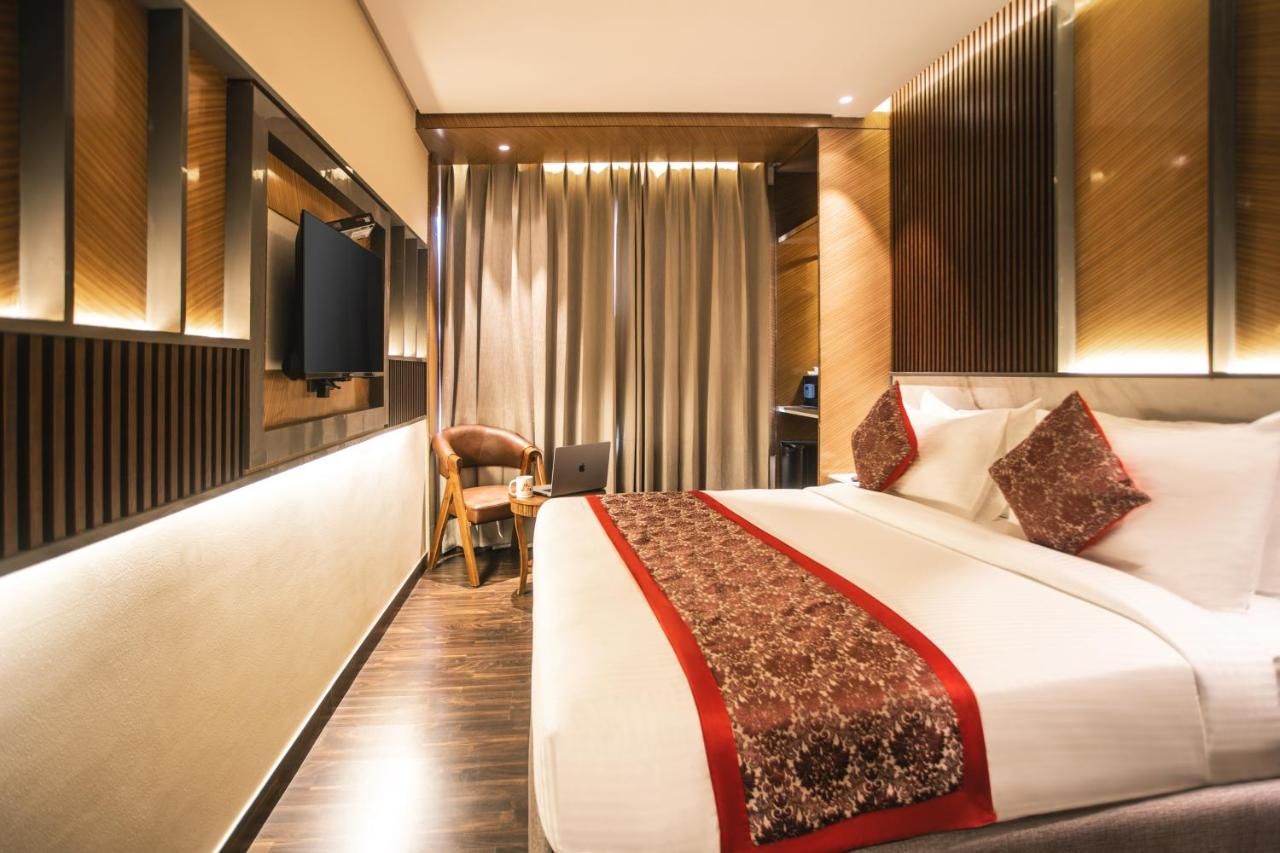 A hotel room with a large bed, a desk with a laptop, a chair, a television, and a curtain.