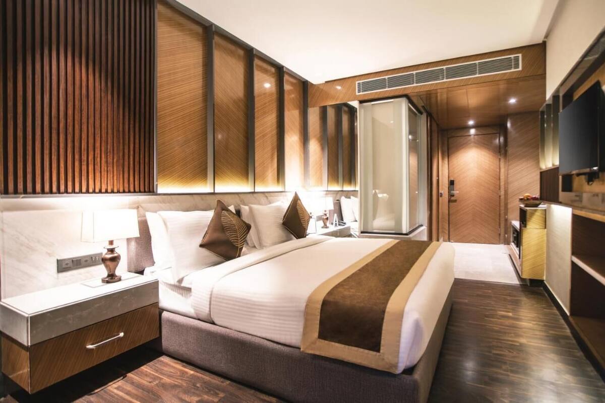 A modern hotel room with a large bed, a bedside table, a wardrobe, and a television.