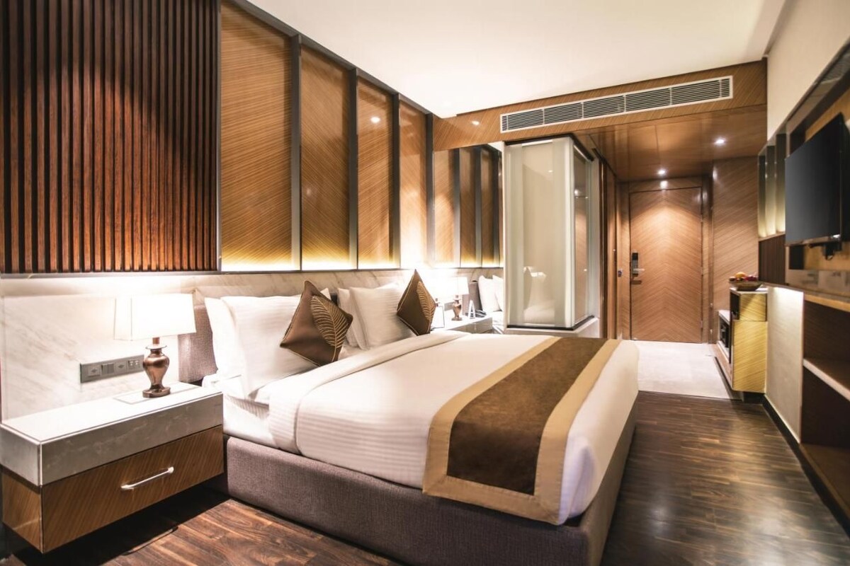 A modern hotel room with a large bed, a bedside table, a wardrobe, and a television.
