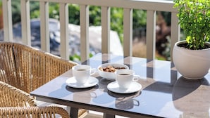 Ein Tisch mit zwei Kaffeetassen und einer Schüssel Kekse, eine Topfpflanze, Korbstühle und Blick auf eine grüne Landschaft.