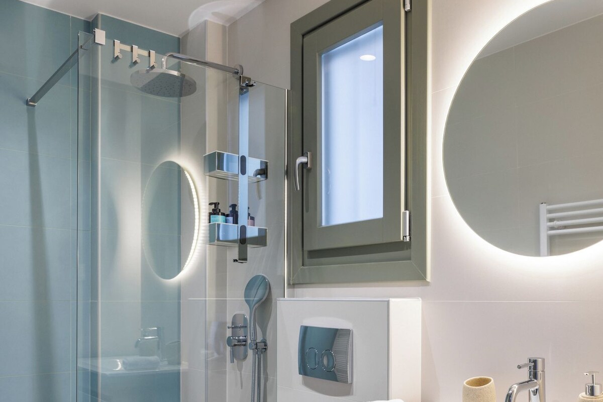 A modern bathroom with a glass shower enclosure, a toilet, a vanity with a mirror, and a built-in heater.