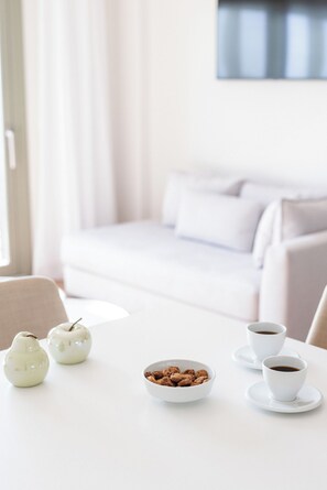 Una habitación minimalista con una mesa blanca, dos tazas blancas, un cuenco de frutos secos y dos objetos cerámicos blancos.