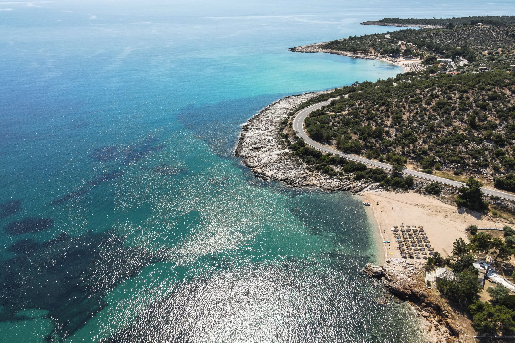 Une zone côtière comprenant une plage, une côte rocheuse et une route qui longe la côte en suivant ses courbes.