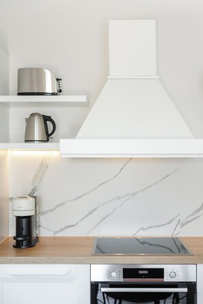 Uma cozinha moderna com exaustor embutido, máquina de café e chaleira de aço inoxidável sobre uma bancada branca.