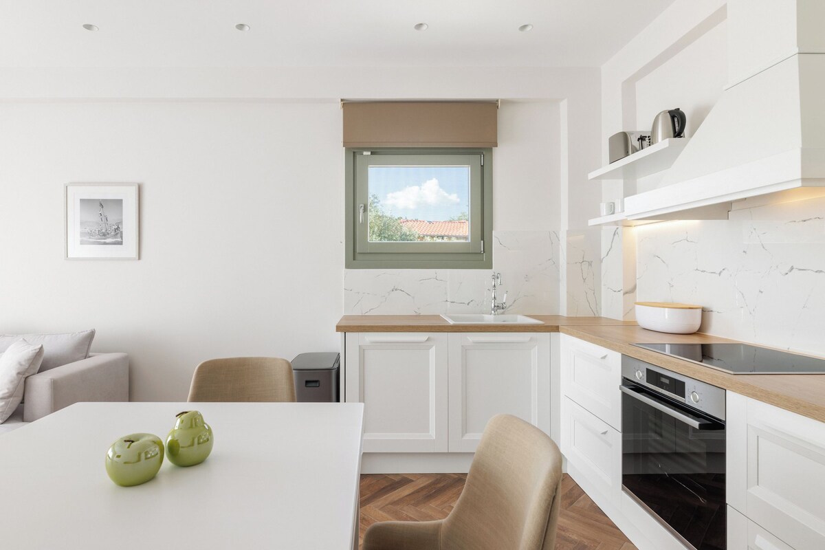 A modern kitchen with white cabinets, a wooden countertop, a built-in oven, and a window with a view.