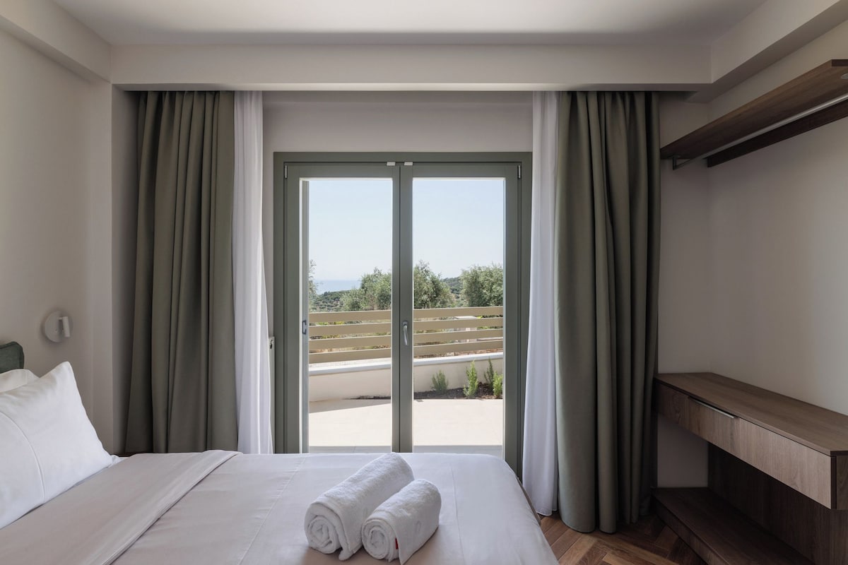 A hotel room with a bed, a bench, and a view through a sliding door.