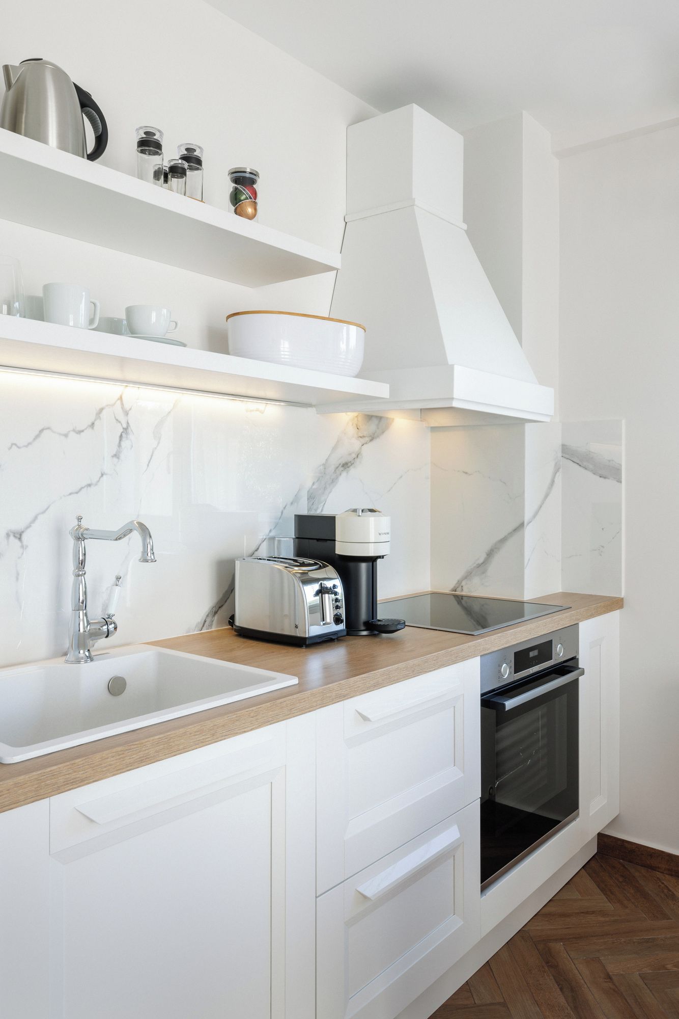 Eine moderne Küche mit weißen Schränken, einer Marmor-Spritzschutzwand, einem Einbauofen und einer Kaffeemaschine.