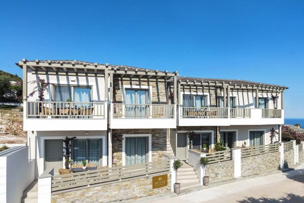 A multi-story building with balconies, stone facade, and a clear view of the sea.