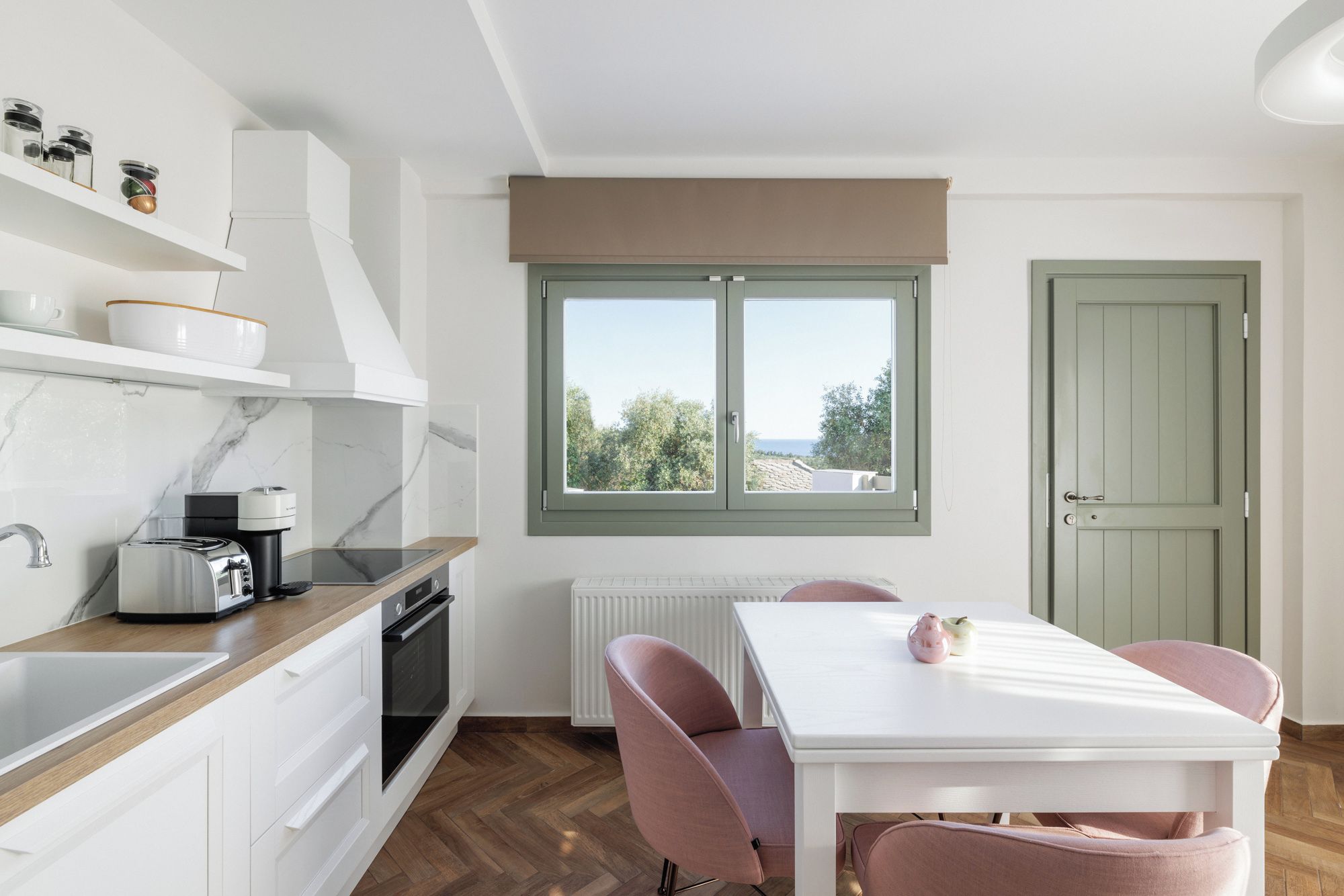 Una cocina moderna con vistas, armarios blancos, una mesa de comedor con sillas y una puerta verde.