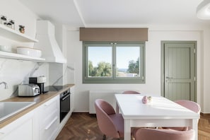 A modern kitchen with a view, white cabinets, a dining table with chairs, and a green door.