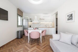 A modern kitchen with white cabinets, a marble countertop, and a dining area with a white table and pink chairs.