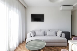 A modern living room with a sofa, a round table, and a flat-screen TV mounted on the wall.