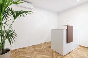 A modern room with a herringbone wood floor, a white wall with a geometric pattern, a white air conditioning unit, a potted plant, and a wooden accent on a white cabinet.