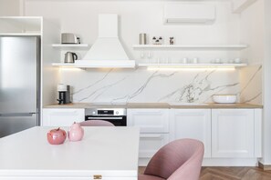 A modern kitchen with white cabinetry, a marble backsplash, and a stainless steel refrigerator.
