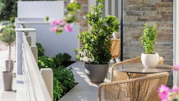 A modern outdoor seating area with wicker chairs and a table, surrounded by potted plants and a stone wall.