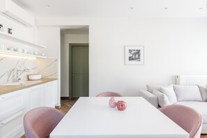 A modern living room with a white table, pink chairs, a white sofa, and a green door.