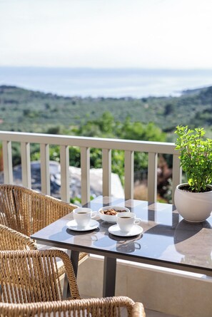 A table with two cups of coffee and a bowl of cookies, a potted plant, wicker chairs, and a view of a green landscape. - Helia All Seasons Apartments (Thasos)