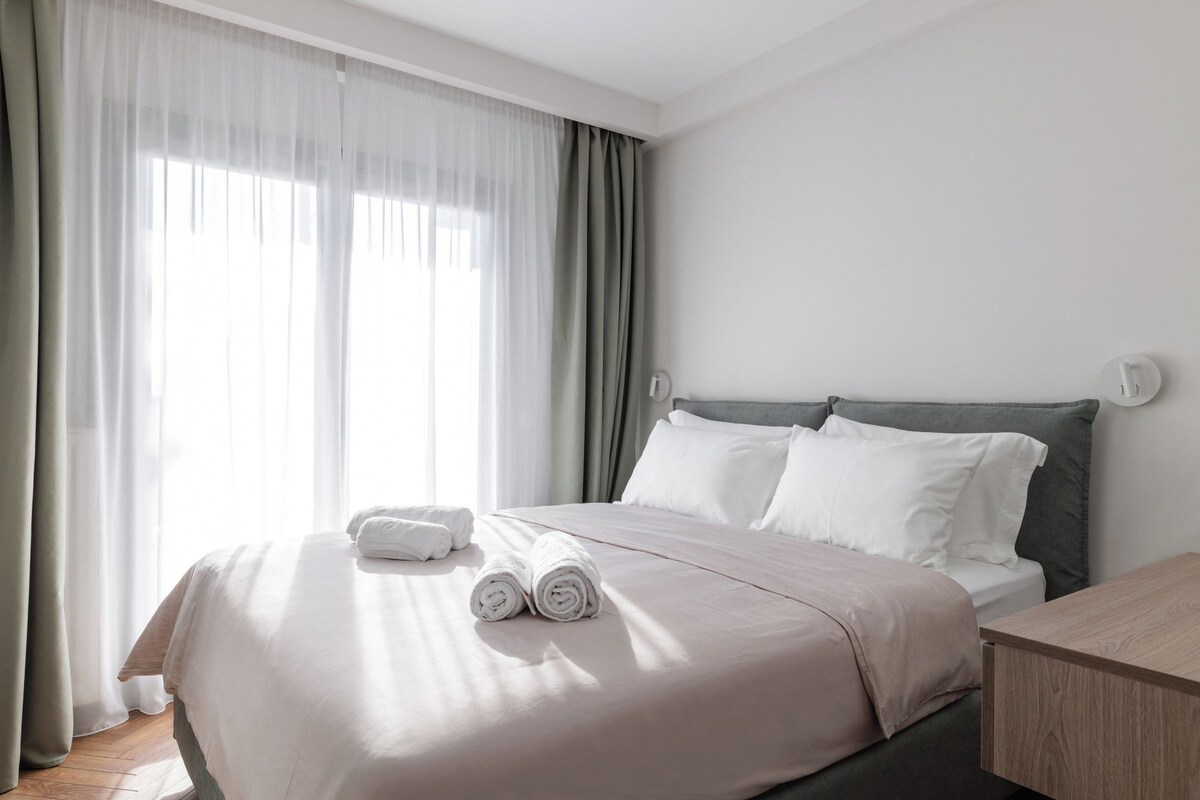 A hotel room with a bed, a bedside table, and a window with curtains.