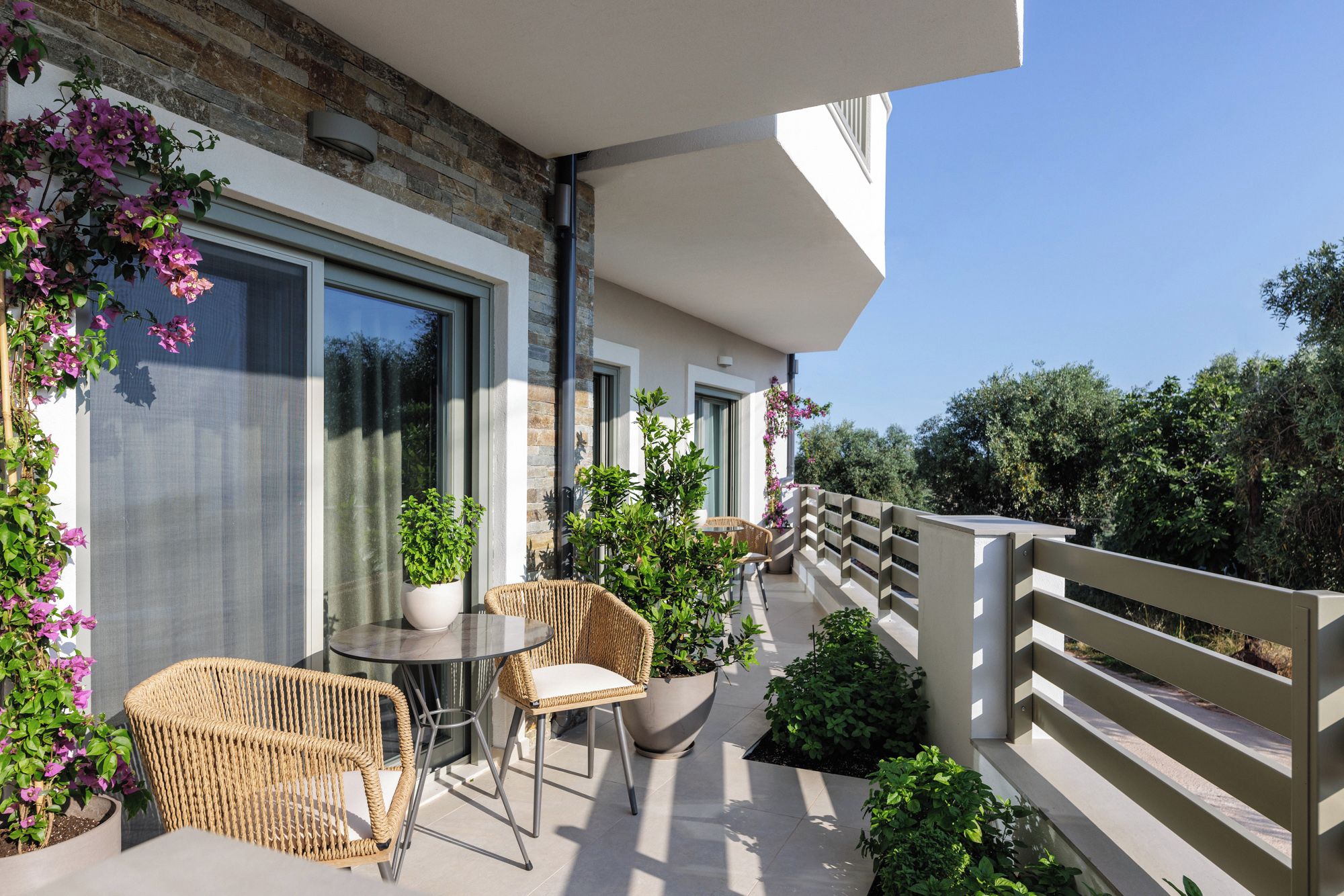 A balcony with wicker furniture, potted plants, and a view of greenery.