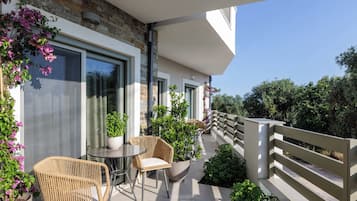 A balcony with wicker furniture, potted plants, and a view of greenery.