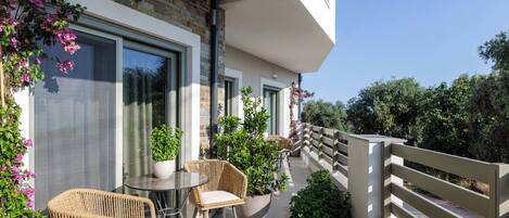 A balcony with wicker furniture, potted plants, and a view of greenery.