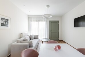 A modern living room with a sofa, a dining table with chairs, a green door, and a mounted TV. - Helia All Seasons Apartments (Thasos)