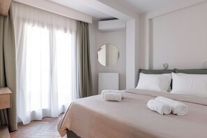 A hotel room with a bed, a round mirror, a radiator, and a window with curtains.