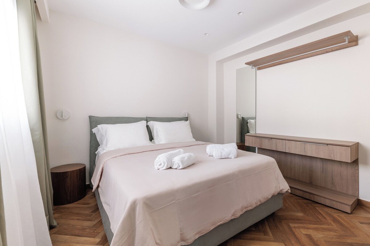A modern bedroom with a bed, bedside table, and a large mirror.