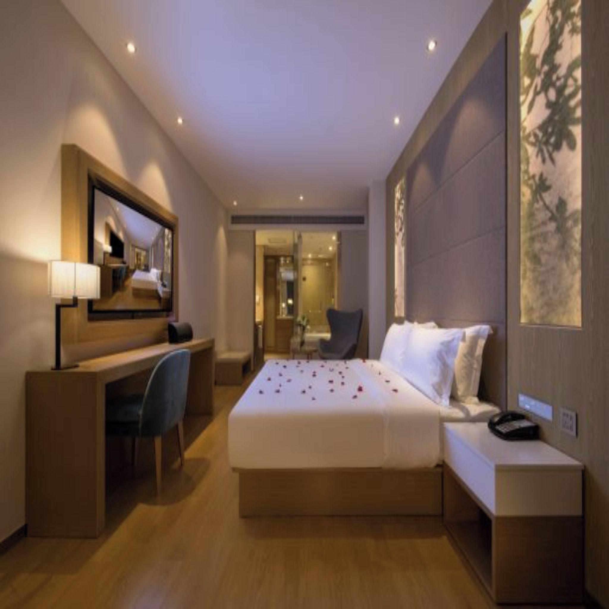 A hotel room with a bed, bedside table, desk, chair, and a large mirror.