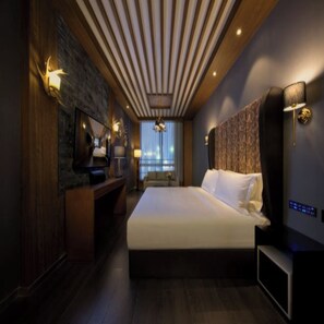 A modern hotel room with a large bed, a TV, a desk, and a city view.