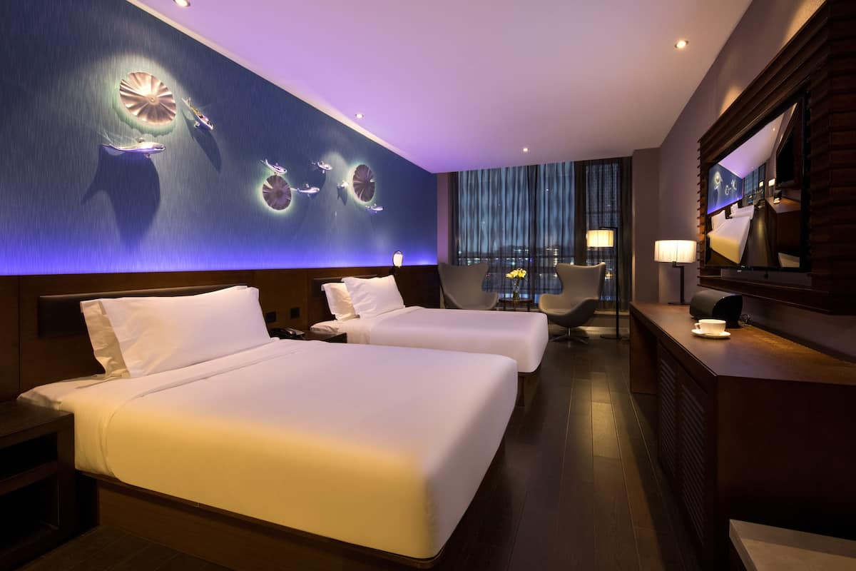 A hotel room with two beds, a desk, a chair, a large mirror, and a wall with circular light fixtures.