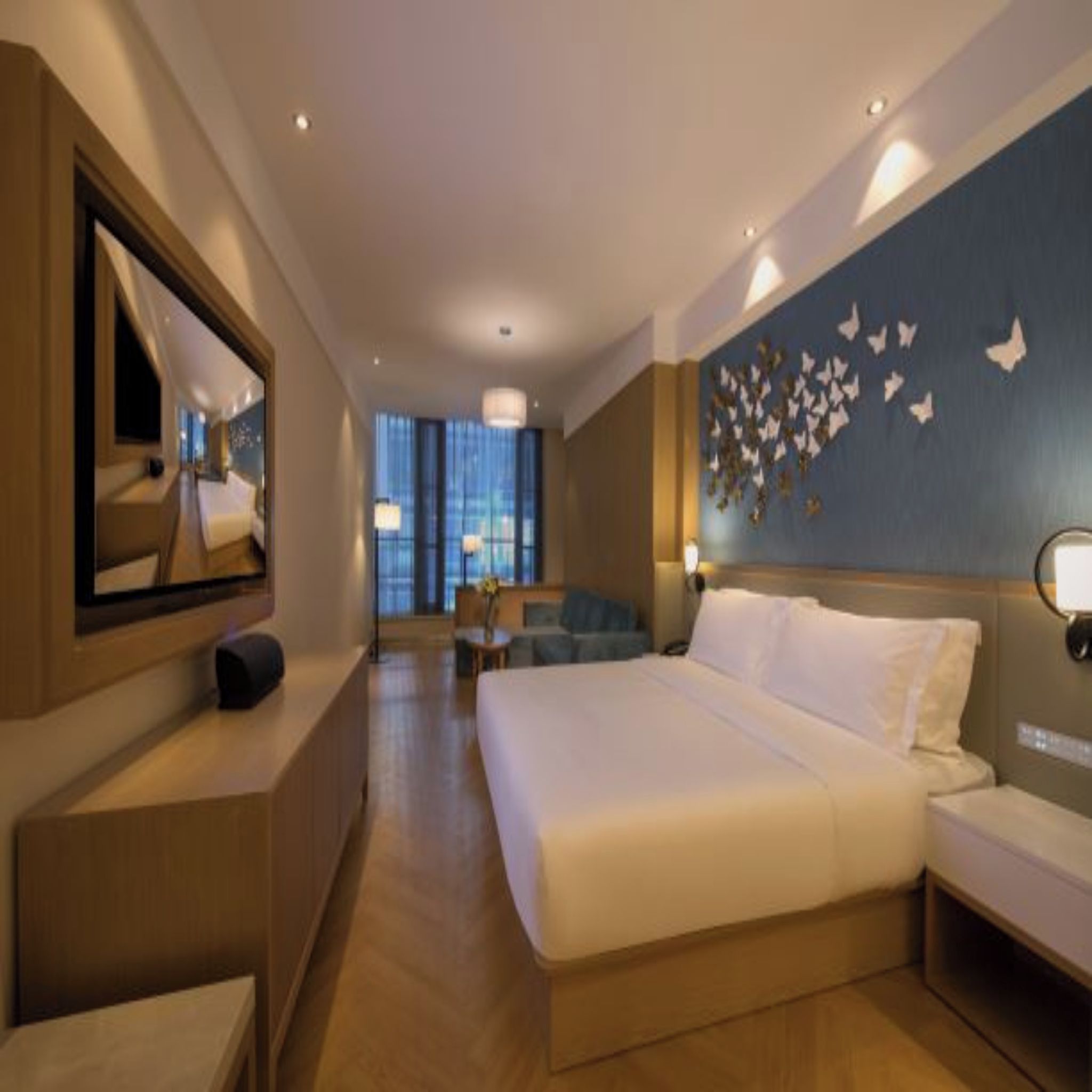 A hotel room with a large bed, a desk, a chair, a mirror, and a wall with butterfly decorations.