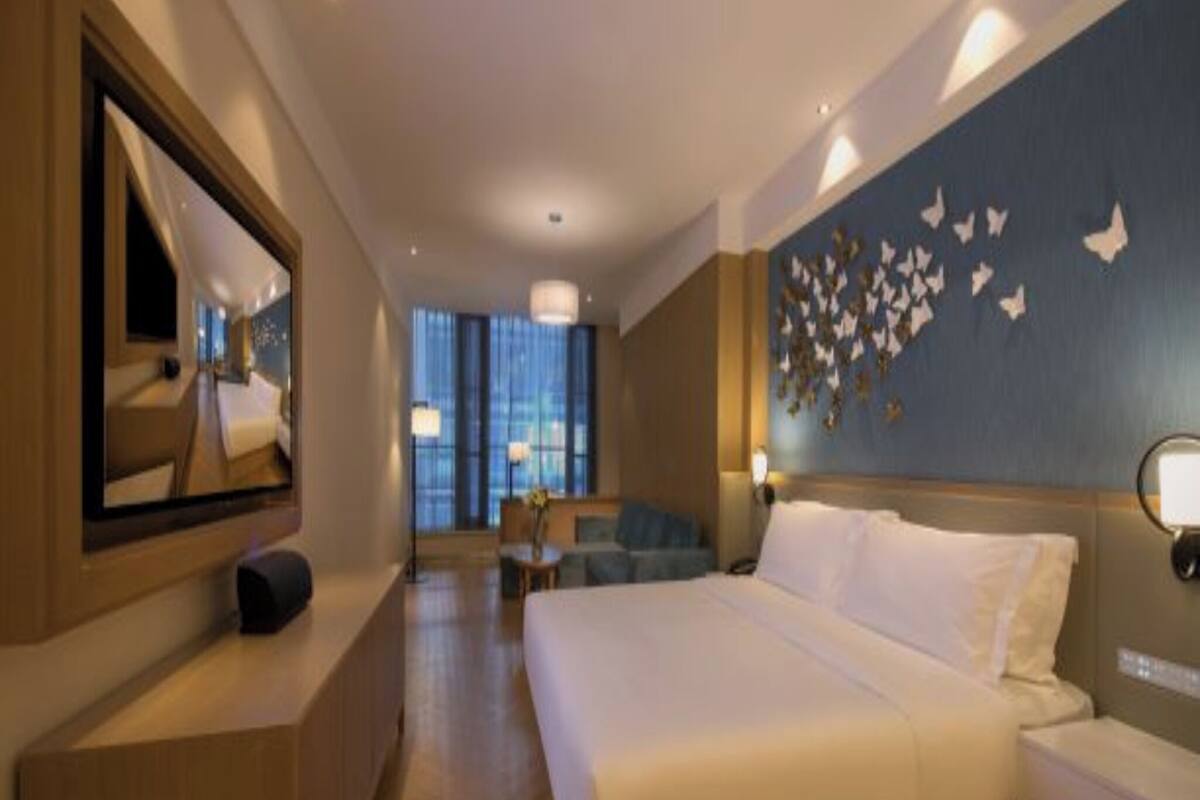 A hotel room with a large bed, a desk, a chair, a mirror, and a wall with butterfly decorations.