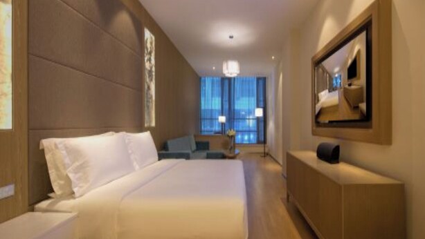 Quarto de hotel moderno com uma cama grande, área de estar, televisão e vista da cidade.
